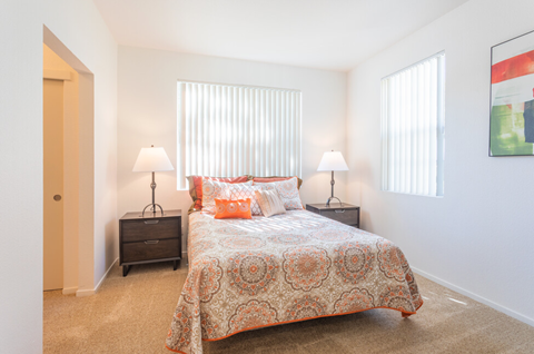 A bedroom with a bed, two lamps, and a painting on the wall at Palm Court Apartments, Salinas