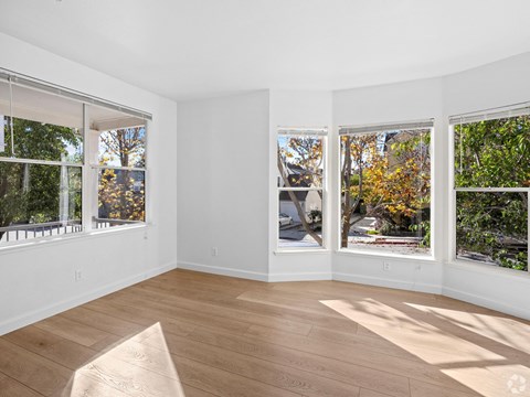A sunny room with a wooden floor and three windows showing trees and a street at Westmont Place Townhomes Apartments, Santa Cruz, CA, 95060