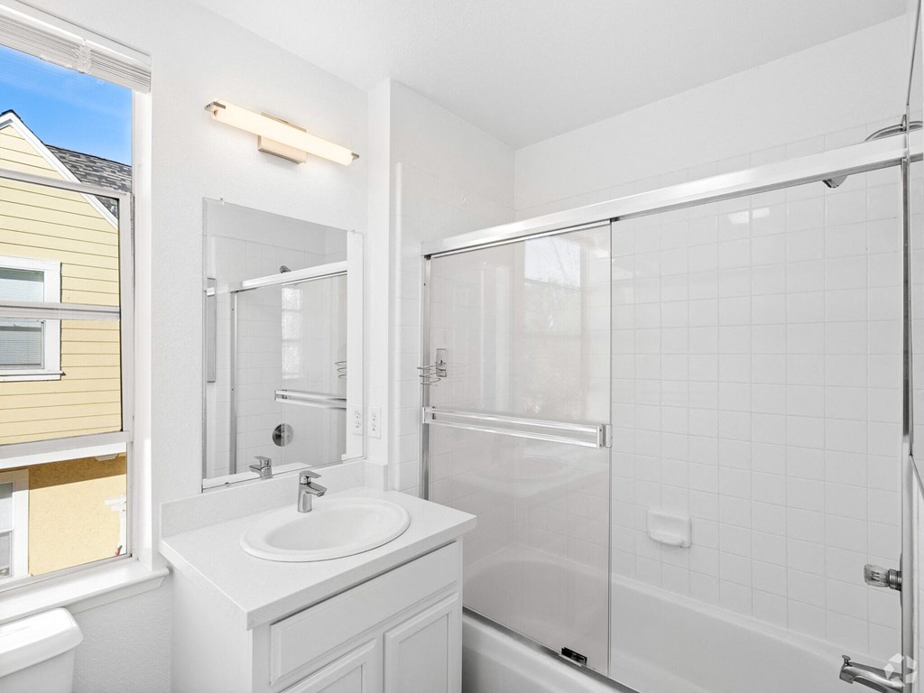 A white bathroom with a sink, mirror, and shower at Westmont Place Townhomes Apartments, Santa Cruz, California