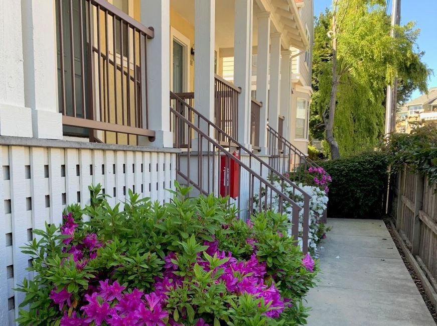 A white house with a red door and a white fence with purple flowers at Westmont Place Townhomes Apartments, Santa Cruz