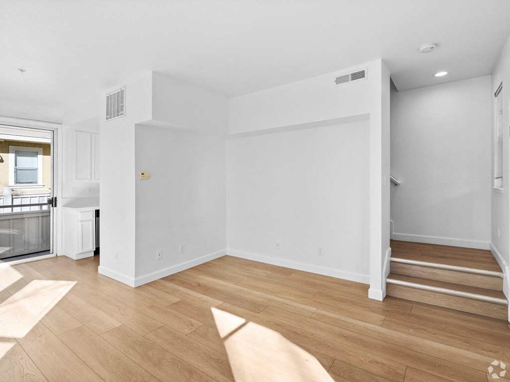 A white room with wooden flooring and a staircase on the right side at Westmont Place Townhomes Apartments, Santa Cruz, 95060
