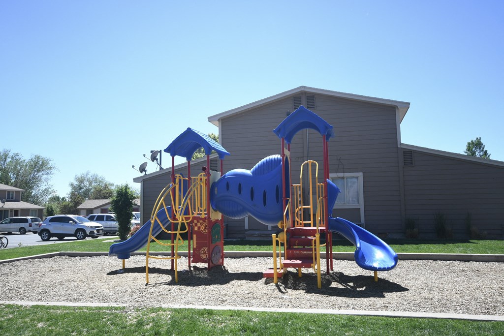 a playground with a blue and red playset in front of a building