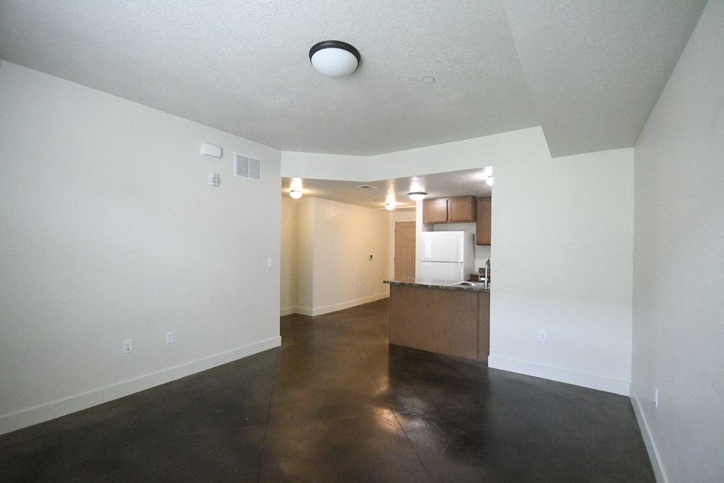 an empty living room with white walls and a kitchen