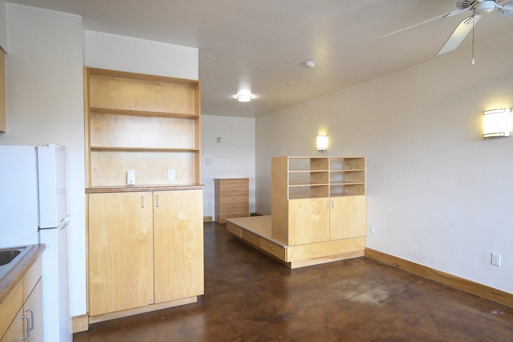 an empty living room with a kitchen and a refrigerator