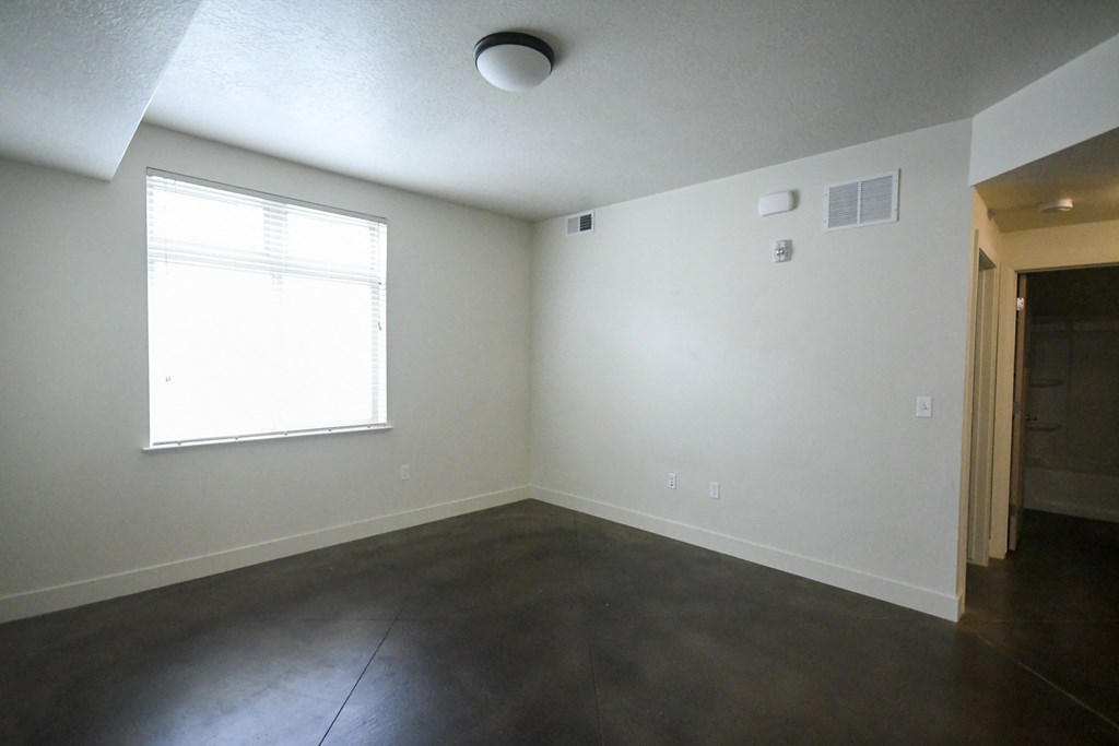 an empty living room with a window and concrete floor