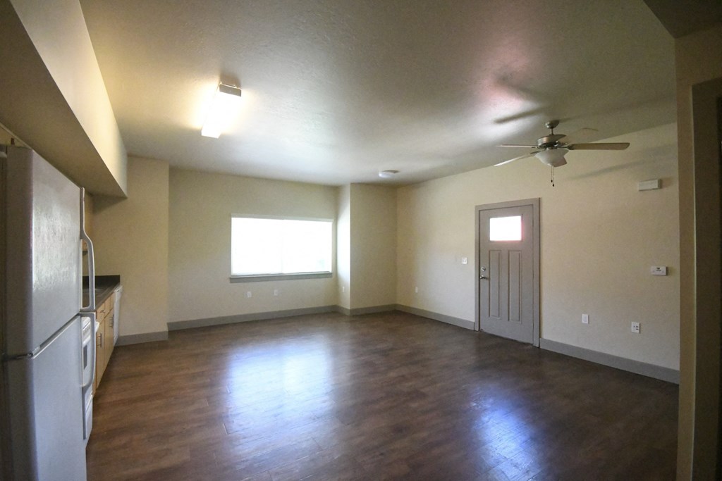an empty living room with a kitchen and a ceiling fan