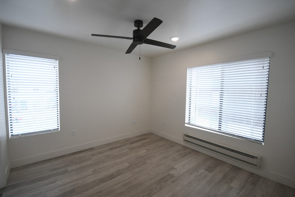 an empty living room with a ceiling fan and two windows