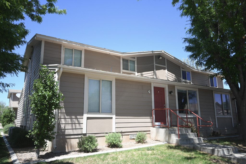 the front of a tan house with a red door