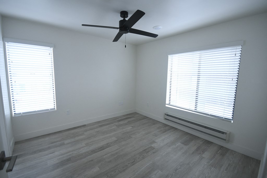 an empty room with a ceiling fan and two windows