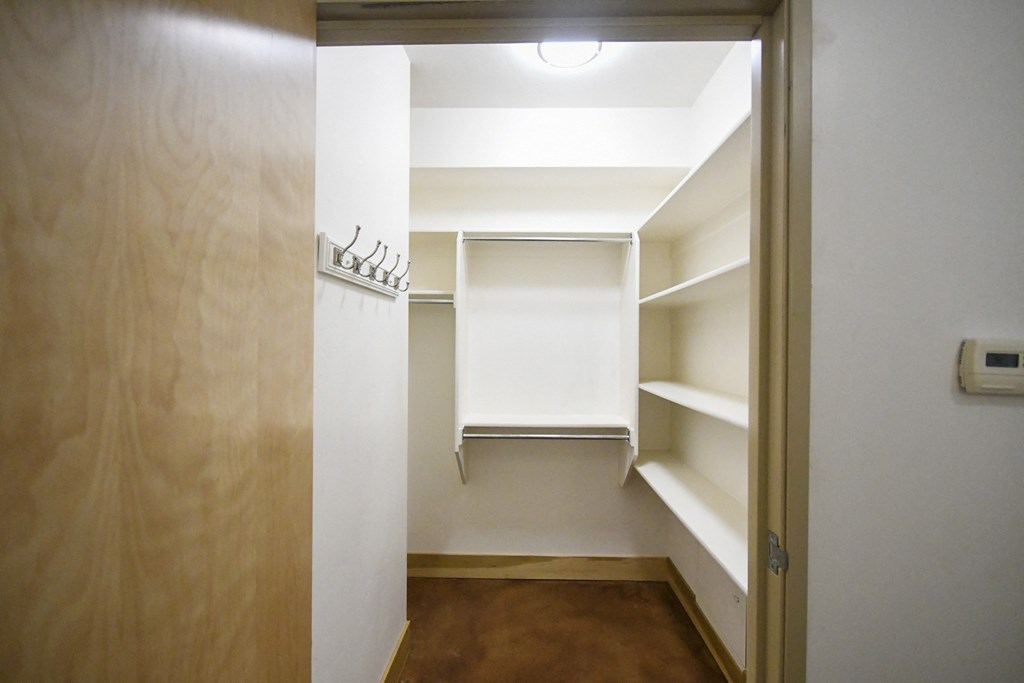 a walk in closet with white shelves and a ceiling light