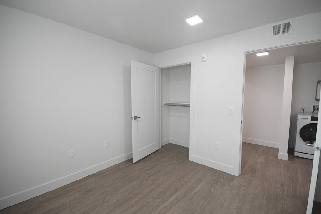 a bedroom with white walls and wood flooring and a laundry room