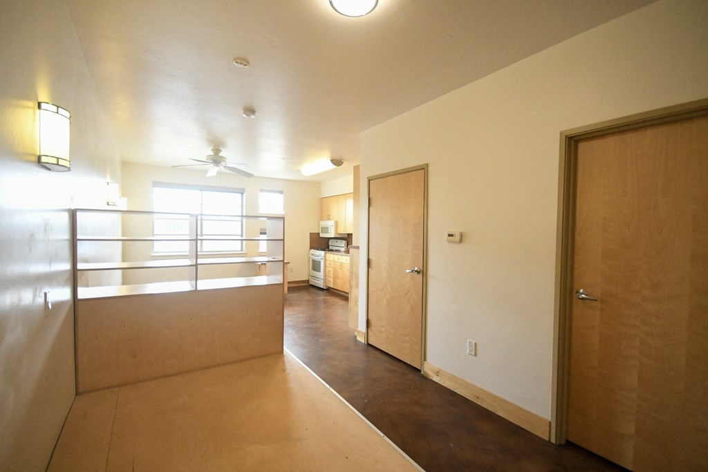 an empty living room with a door to a bedroom and a kitchen