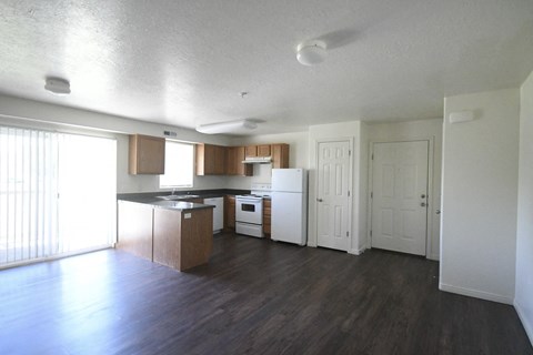 an empty living room and kitchen with wood floors and white appliances