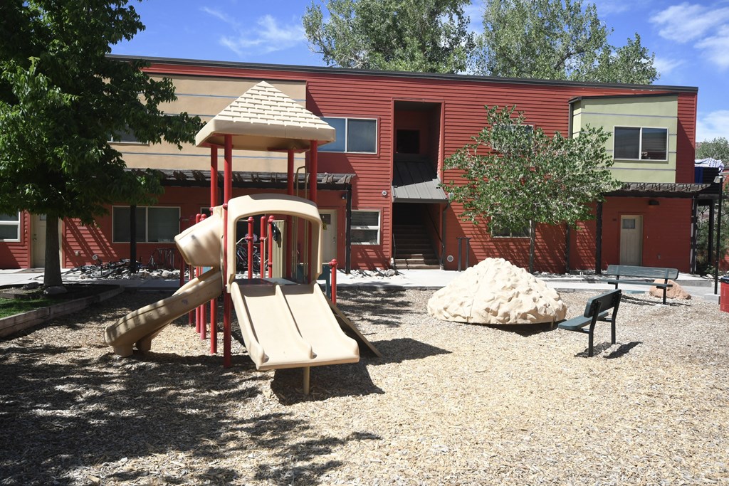 a playground with a slide in front of a red building