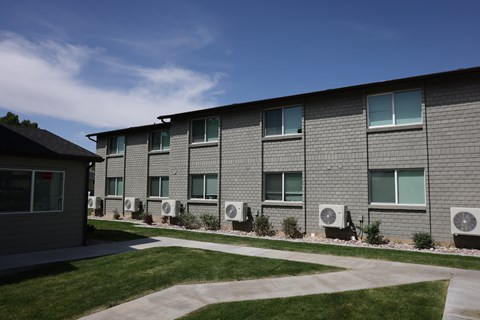 A building with grey walls and multiple air conditioning units in front.