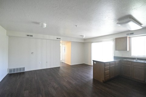 an empty living room and kitchen with wood floors and white walls
