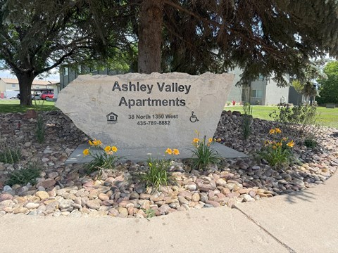 A stone sign for Ashley Valley Apartments sits in front of a tree.