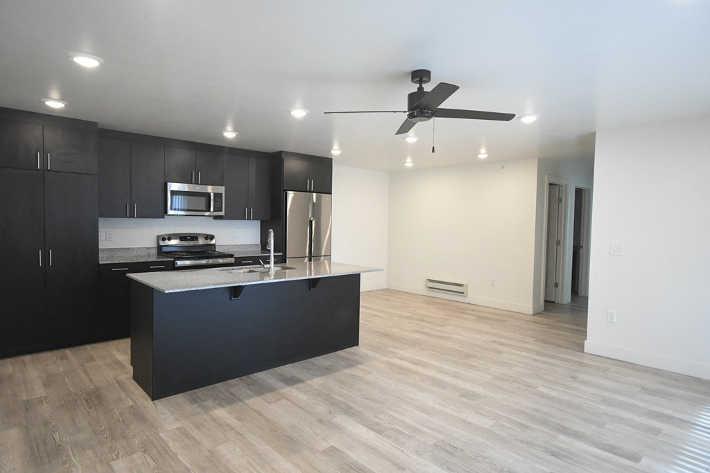an empty living room with a kitchen and a ceiling fan