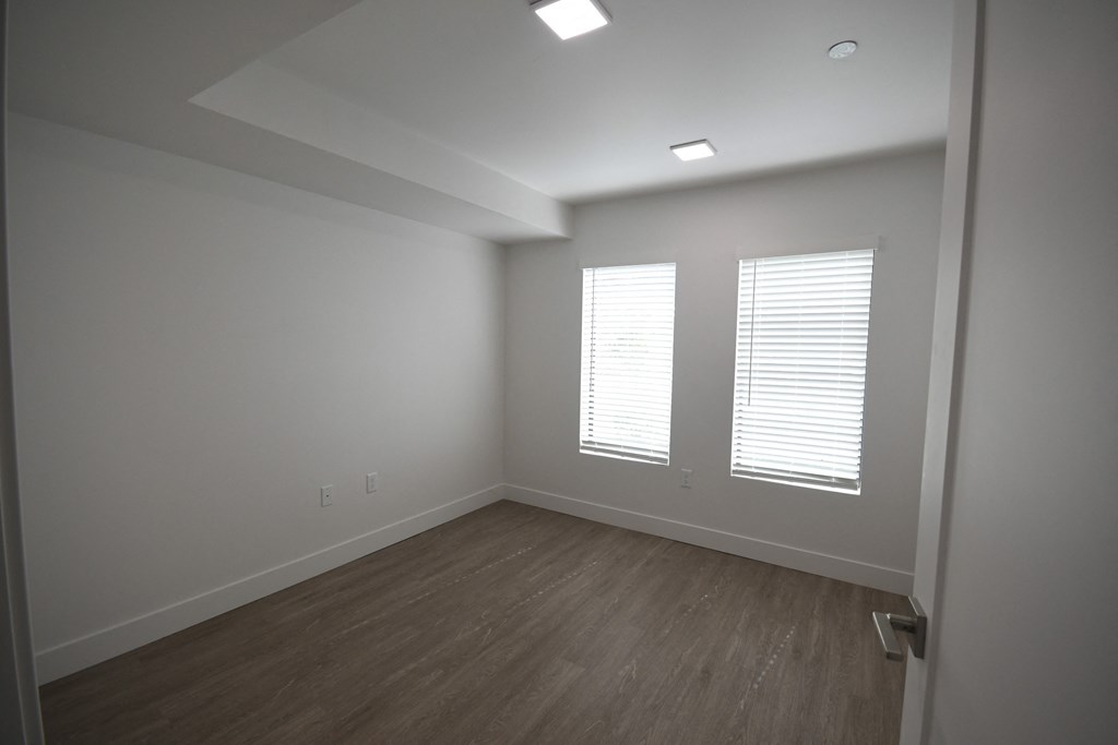 a bedroom with white walls and wooden floors and two windows