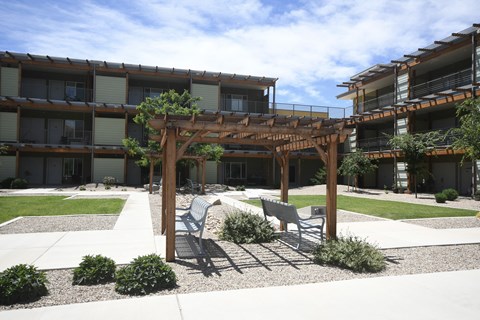 a patio with chairs and a pergola in front of an apartment building
