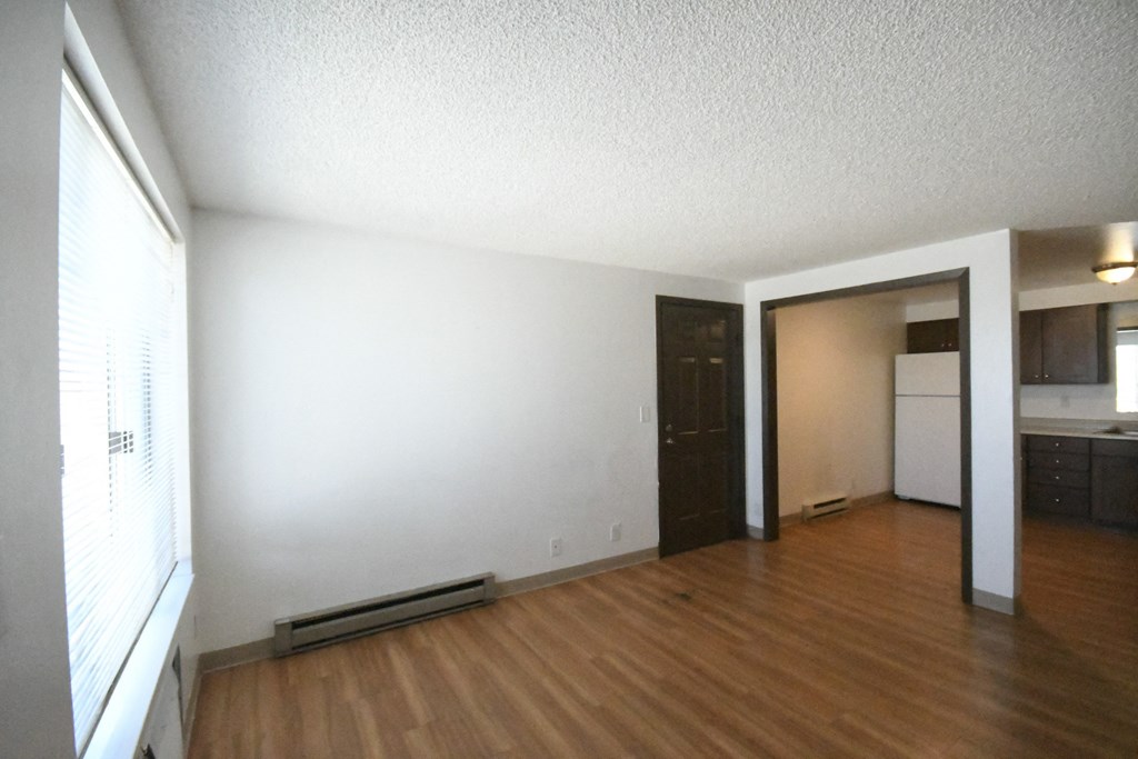 an empty living room with wood floors and a kitchen