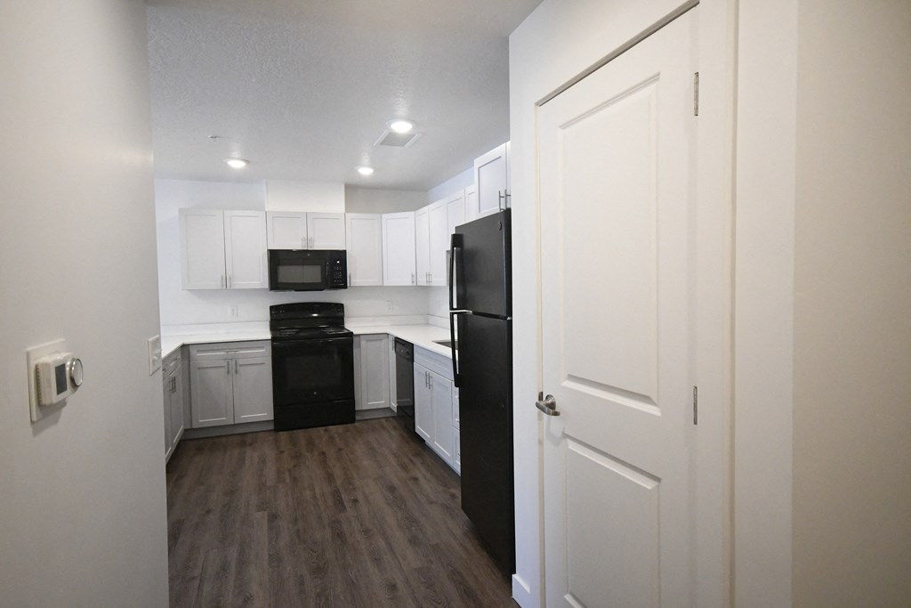 an empty kitchen with white cabinets and a black refrigerator