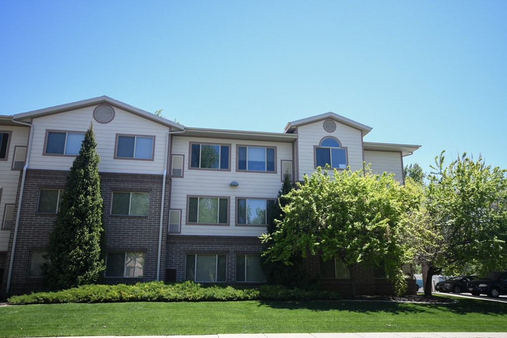 an apartment building with a lawn and trees in front of it