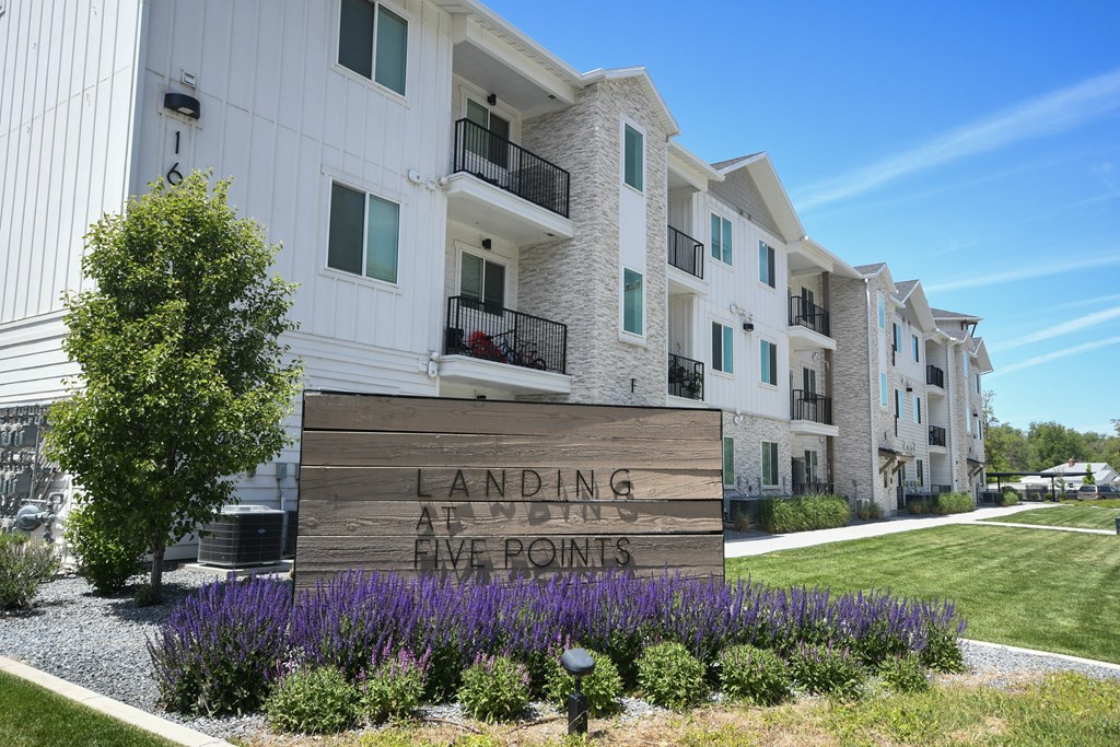 a sign in front of an apartment building with purple flowers