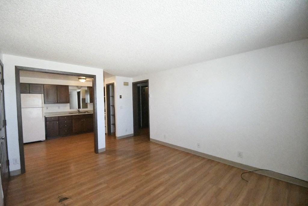 an empty living room with wood floors and a kitchen
