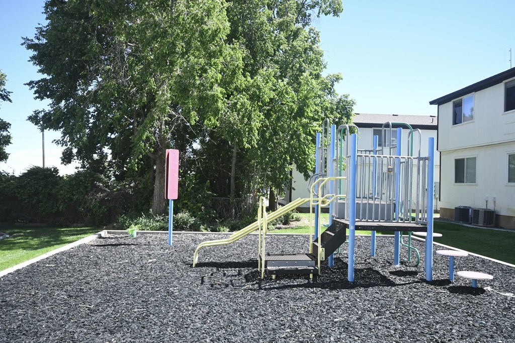 a playground with a bench and slides in front of a tree