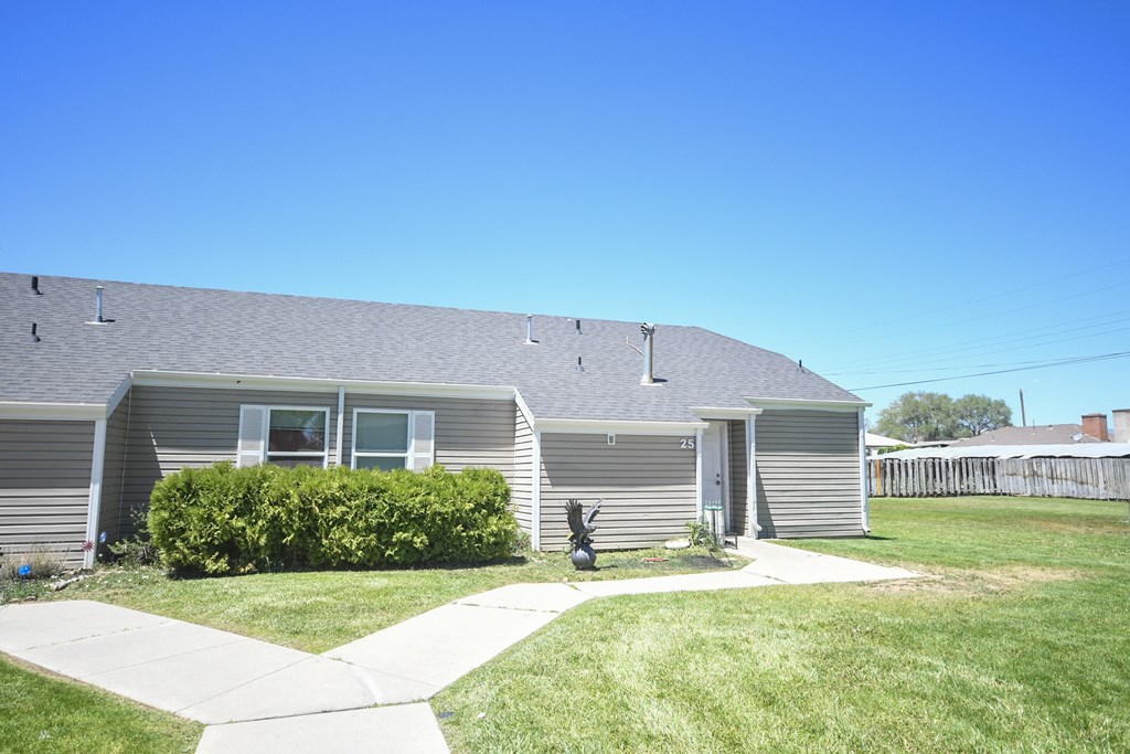 the front of a gray house with a yard and a sidewalk