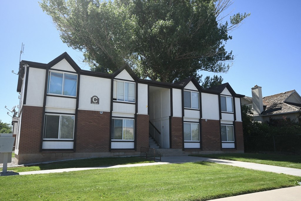 the front of a brick apartment building with a lawn and a tree