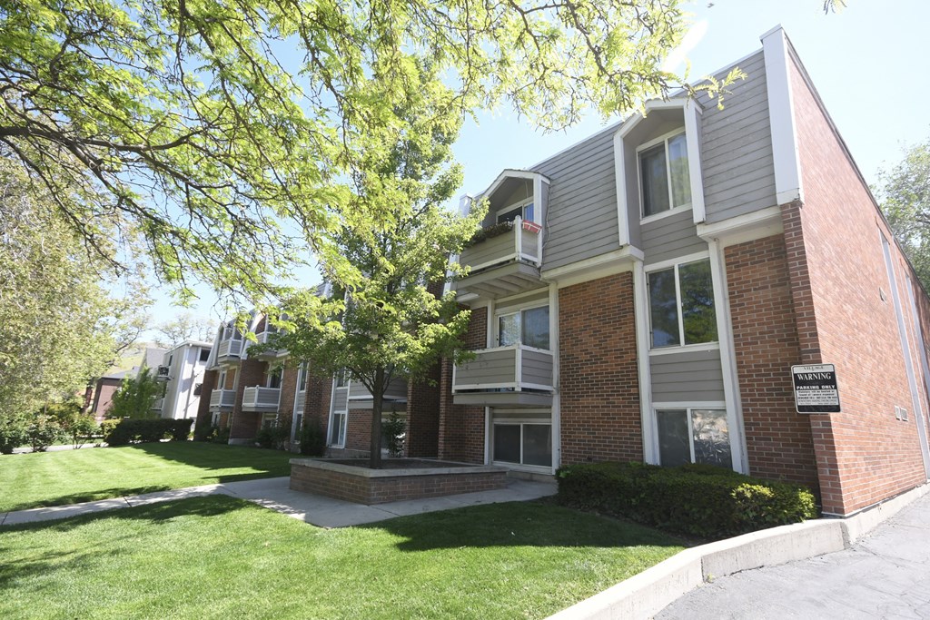 the exterior of an apartment building with a lawn and trees