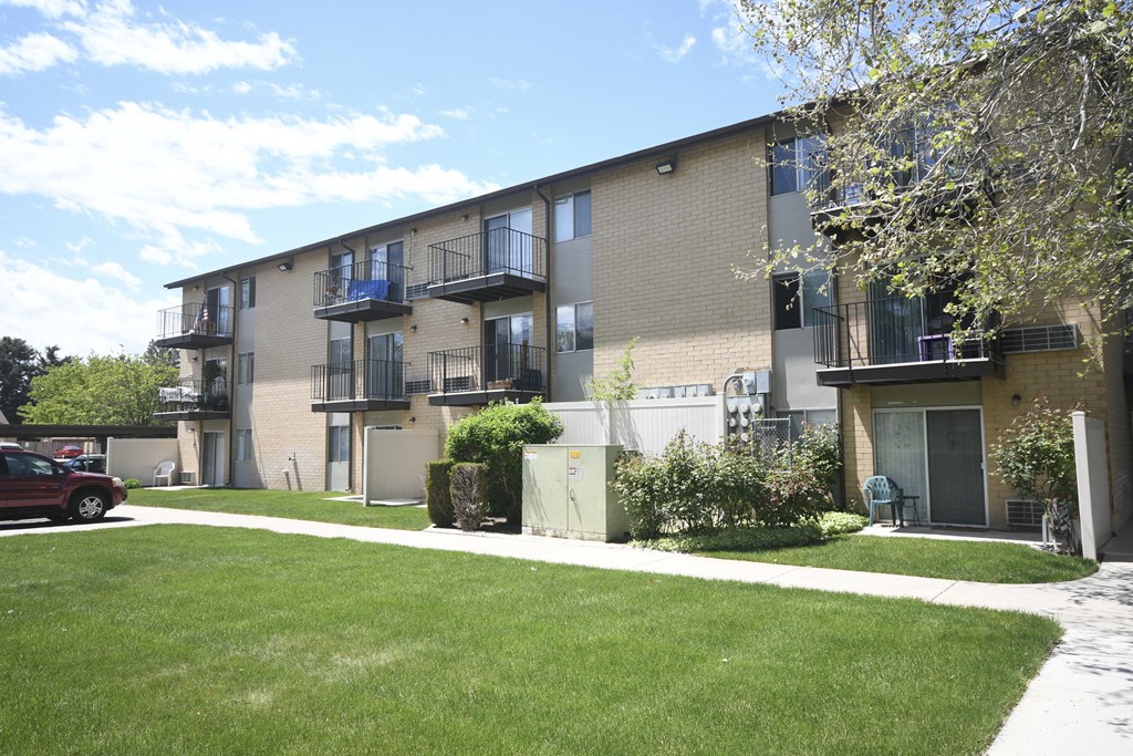 the exterior of an apartment building with green grass and trees
