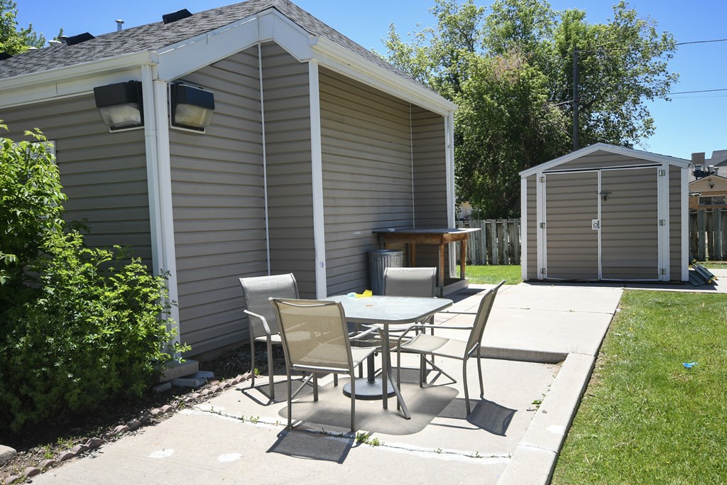 a backyard patio with a table and chairs and a shed