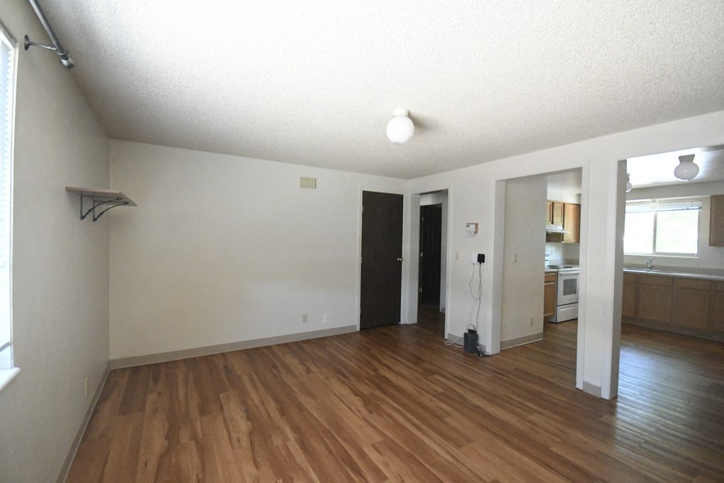 an empty living room with wood flooring and a kitchen