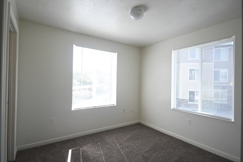 an empty bedroom with two windows and a carpeted floor