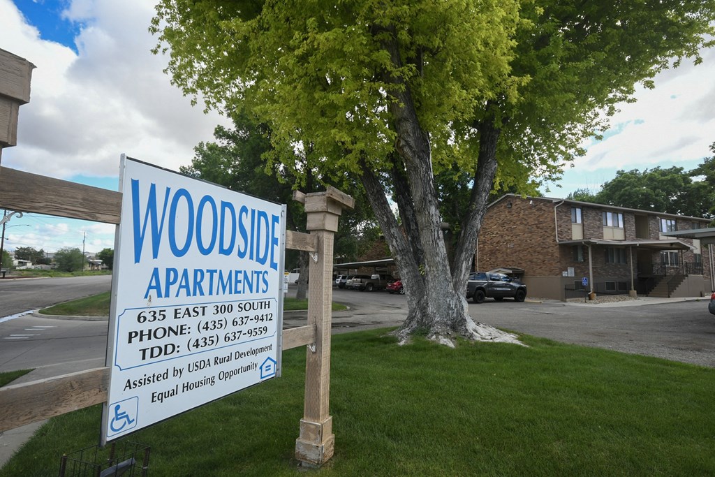 a sign for woods apartments is displayed in front of a tree
