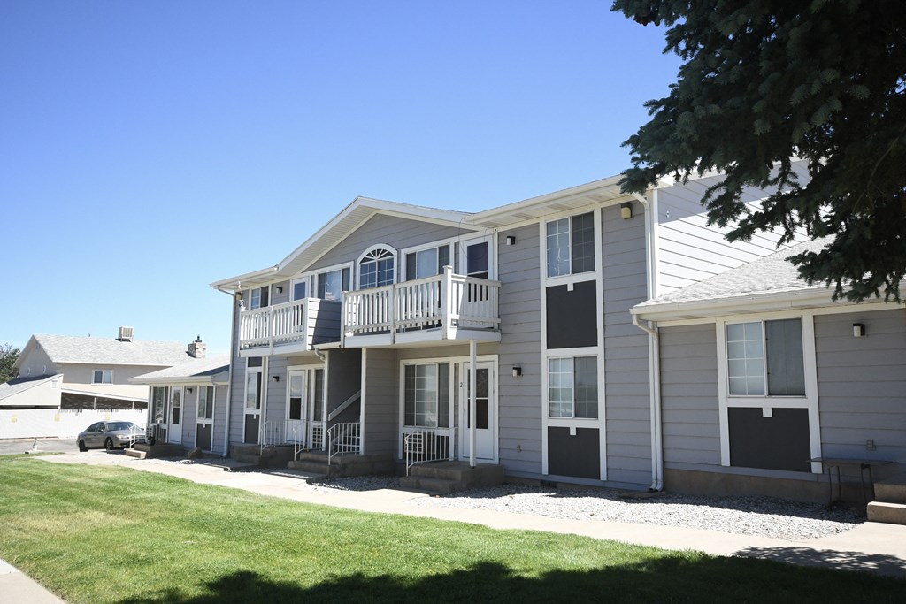 the exterior of an apartment building with a lawn and a tree