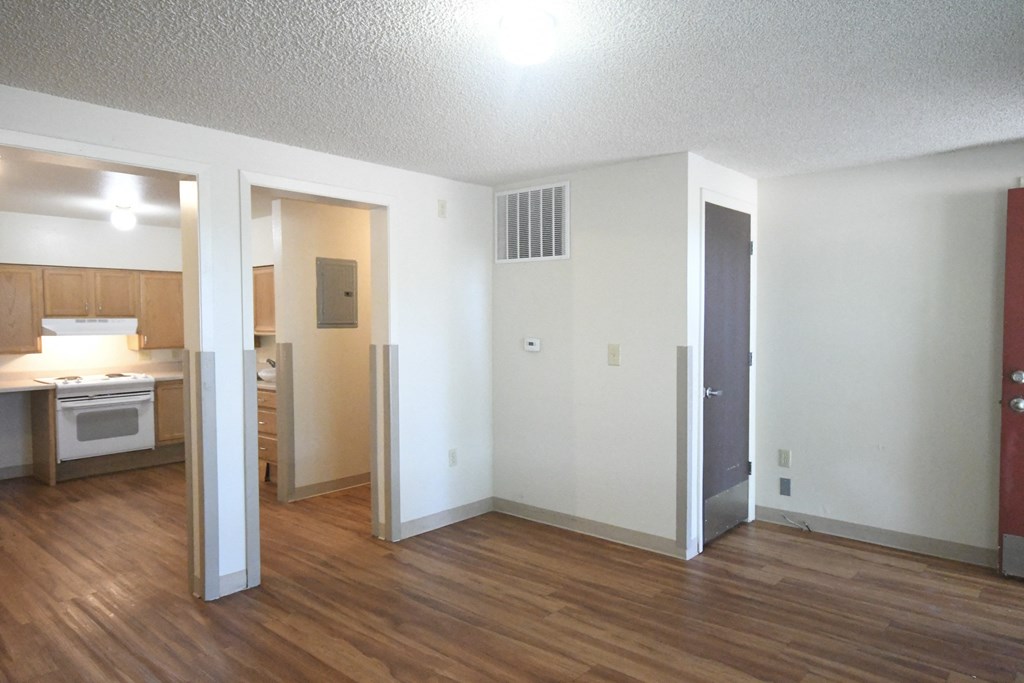 an empty living room and kitchen with wood floors and white walls