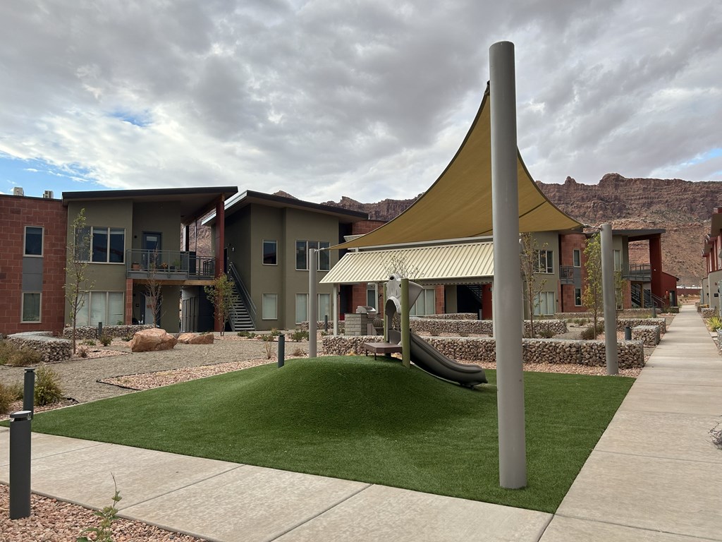 A playground with a yellow canopy and a slide is in front of a building.