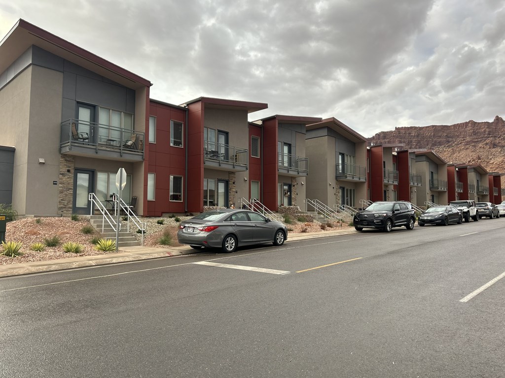 A row of modern apartment buildings with cars parked in front.