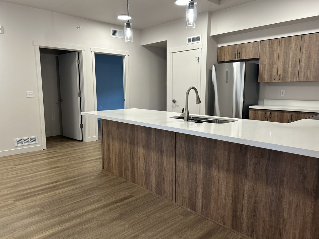A kitchen with a white counter top and wooden flooring.