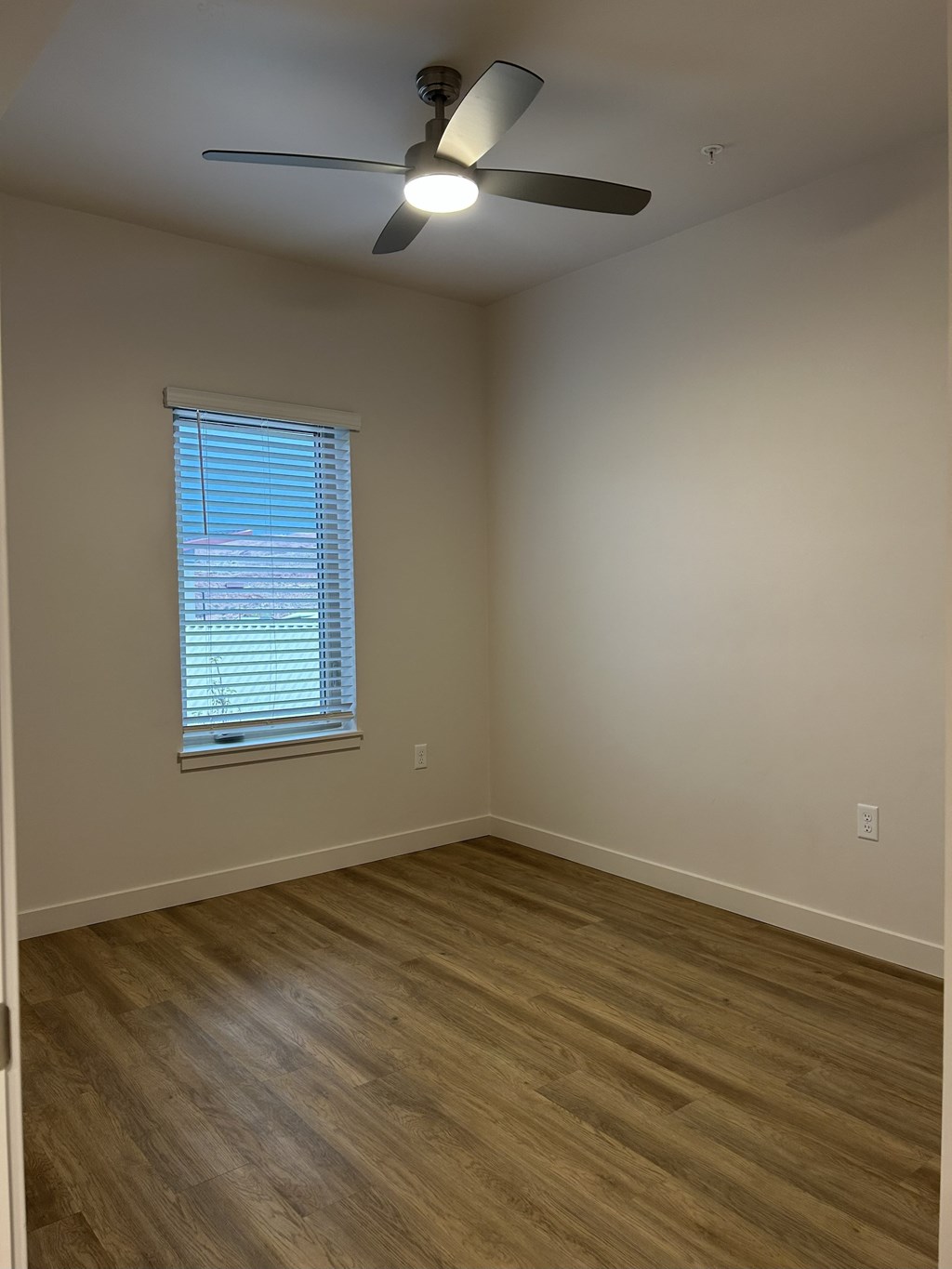 A room with a ceiling fan and a window with blinds.