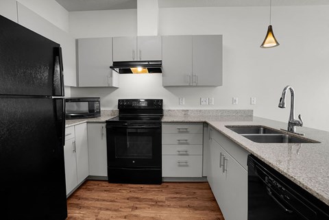 A black refrigerator stands in a kitchen with white cabinets and a black oven.