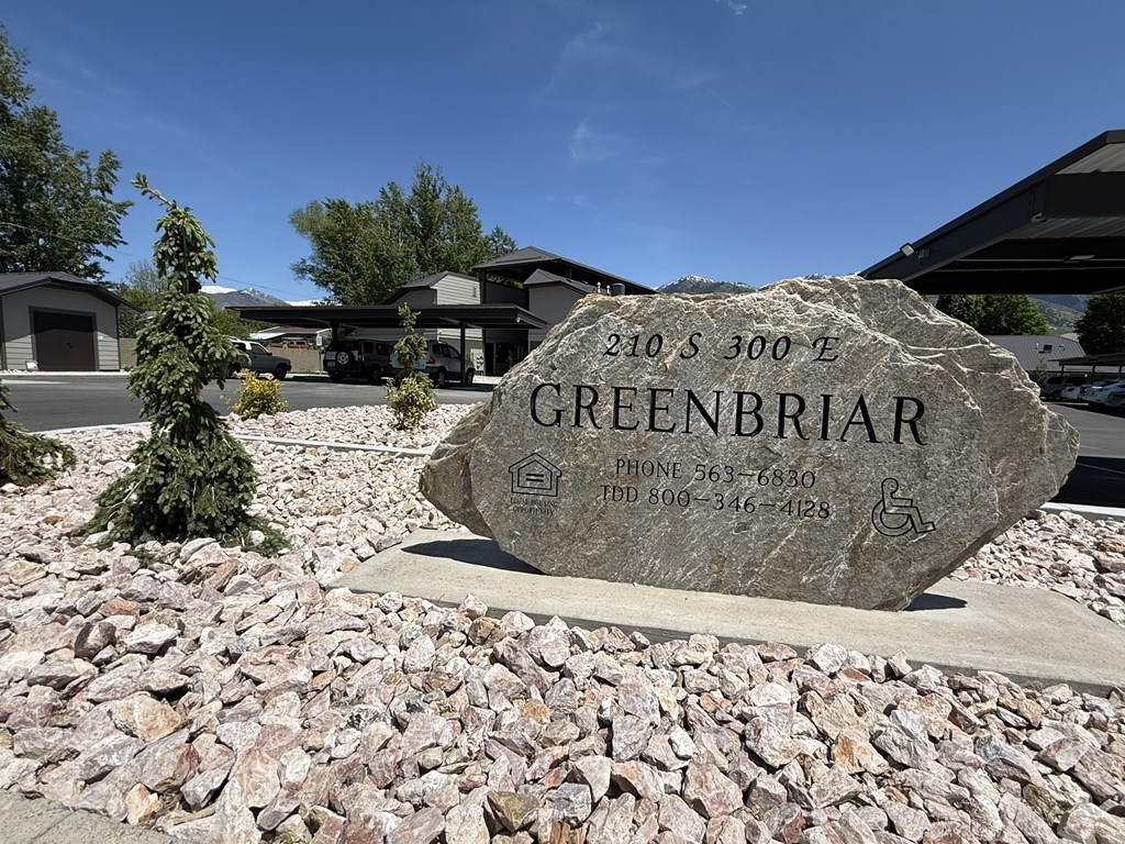A stone sign with the name GREENBRIAR and contact information is in front of a building.