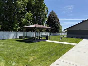 A gazebo sits in the middle of a grassy area with a white fence in the background.