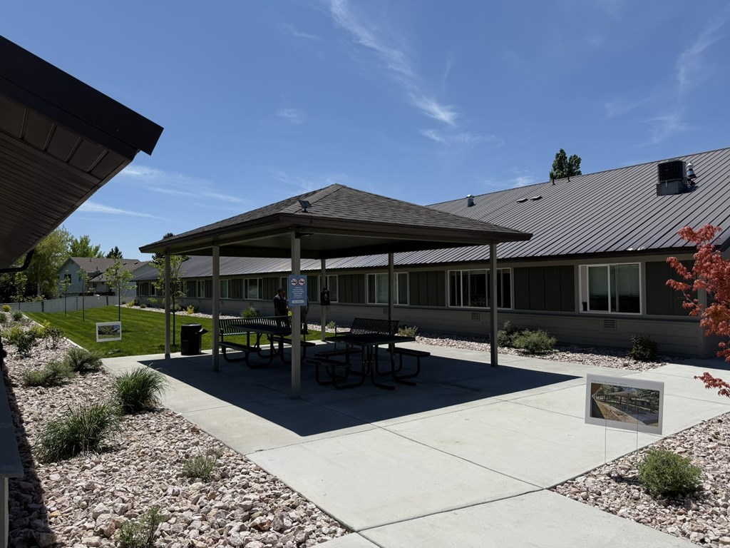 A pavilion with a picnic table is surrounded by gravel and grass.
