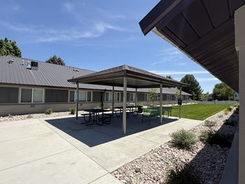 A covered picnic area with tables and benches is located in front of a building.