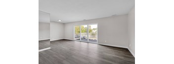 A spacious room with wooden flooring and a view of a patio through the glass door.
